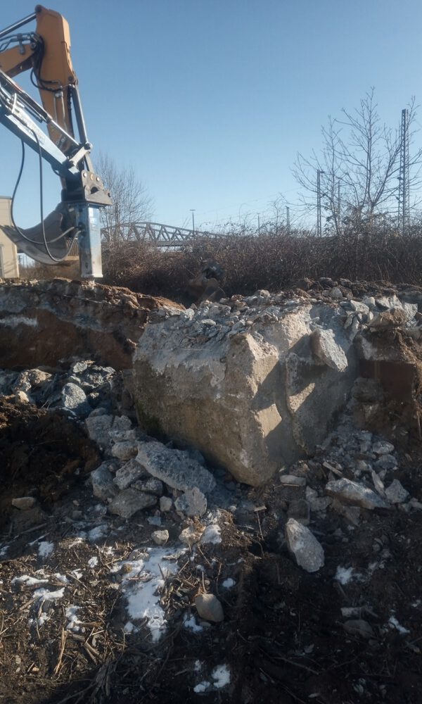 Ein Baufahrzeug mit Meißel zerkleinert einen Betonblock