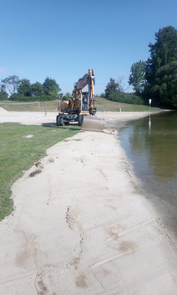 Ein Bagger verteilt Sand auf einem Strand am See